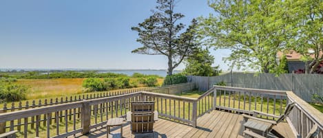 A wooden deck with picnic tables and chairs, overlooking a grassy area and a tree.