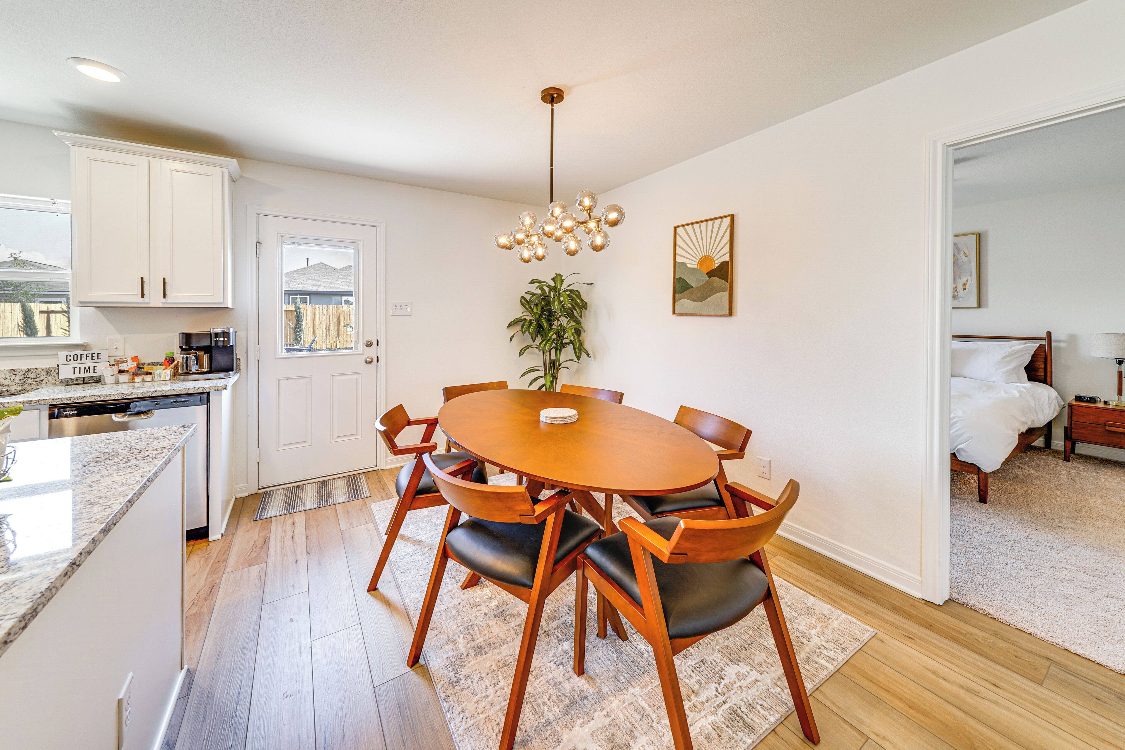 A modern kitchen with white cabinets, a dining table with chairs, a coffee machine, and a potted plant.