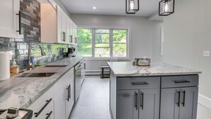 Une cuisine moderne dotée d’un grand îlot central, de meubles de couleur grise et d’une fenêtre qui laisse entrer la lumière naturelle.