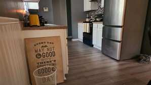 A kitchen with wooden flooring, white cabinets, a stainless steel refrigerator, and a coffee maker.
