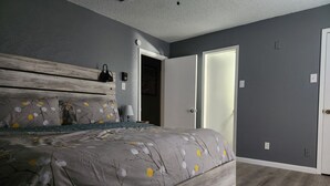 A bedroom with a bed, a nightstand, a lamp, and a door.