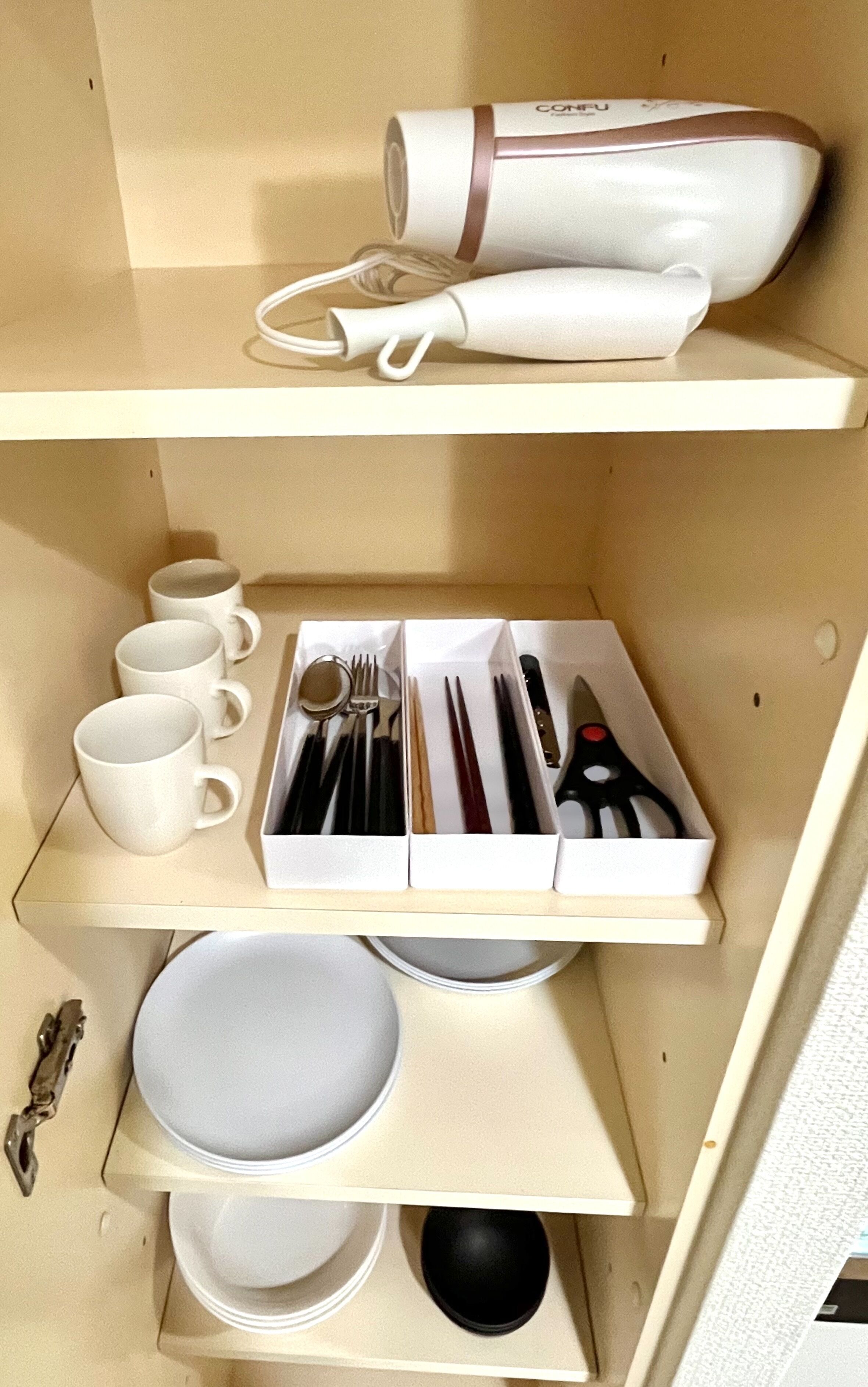 A neatly organized kitchen with white cabinets, a coffee maker, cups, cutlery, and plates.