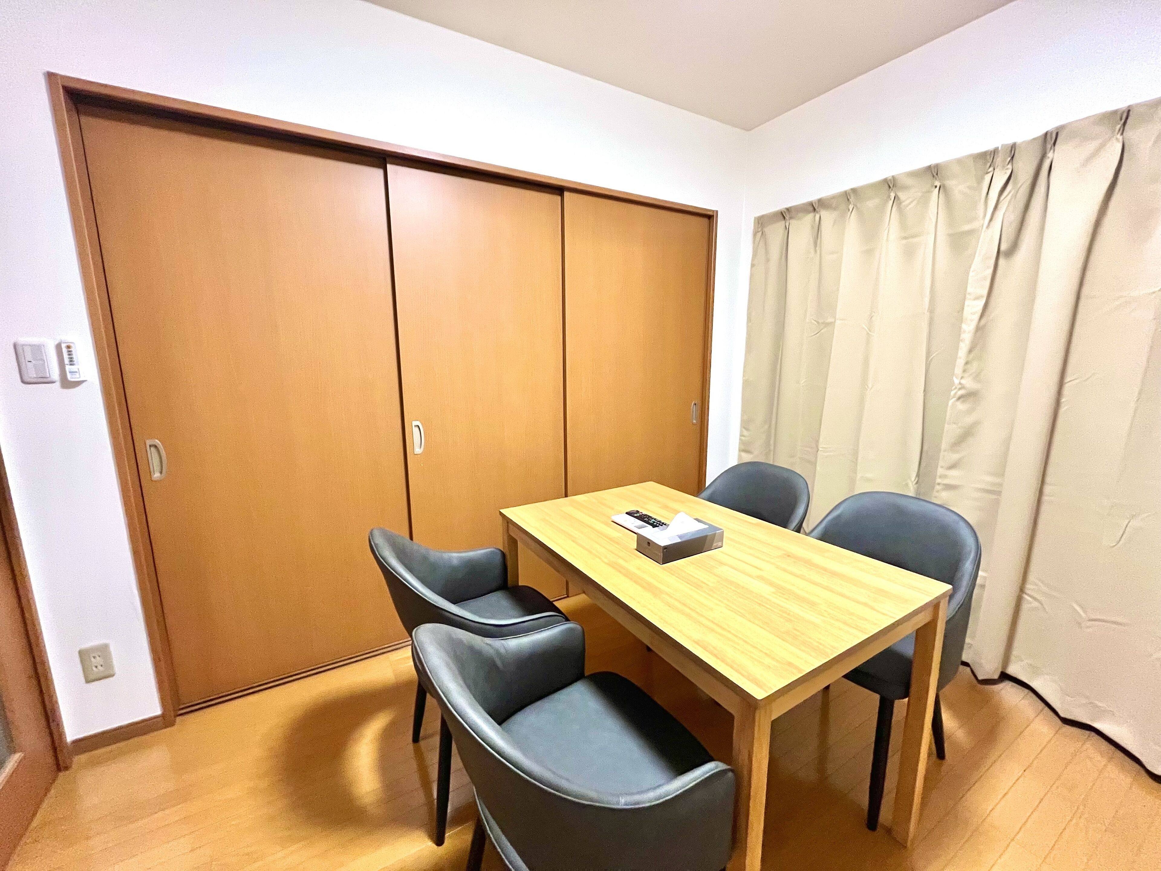 A room with a wooden table and four chairs, a sliding door closet, and a curtain.