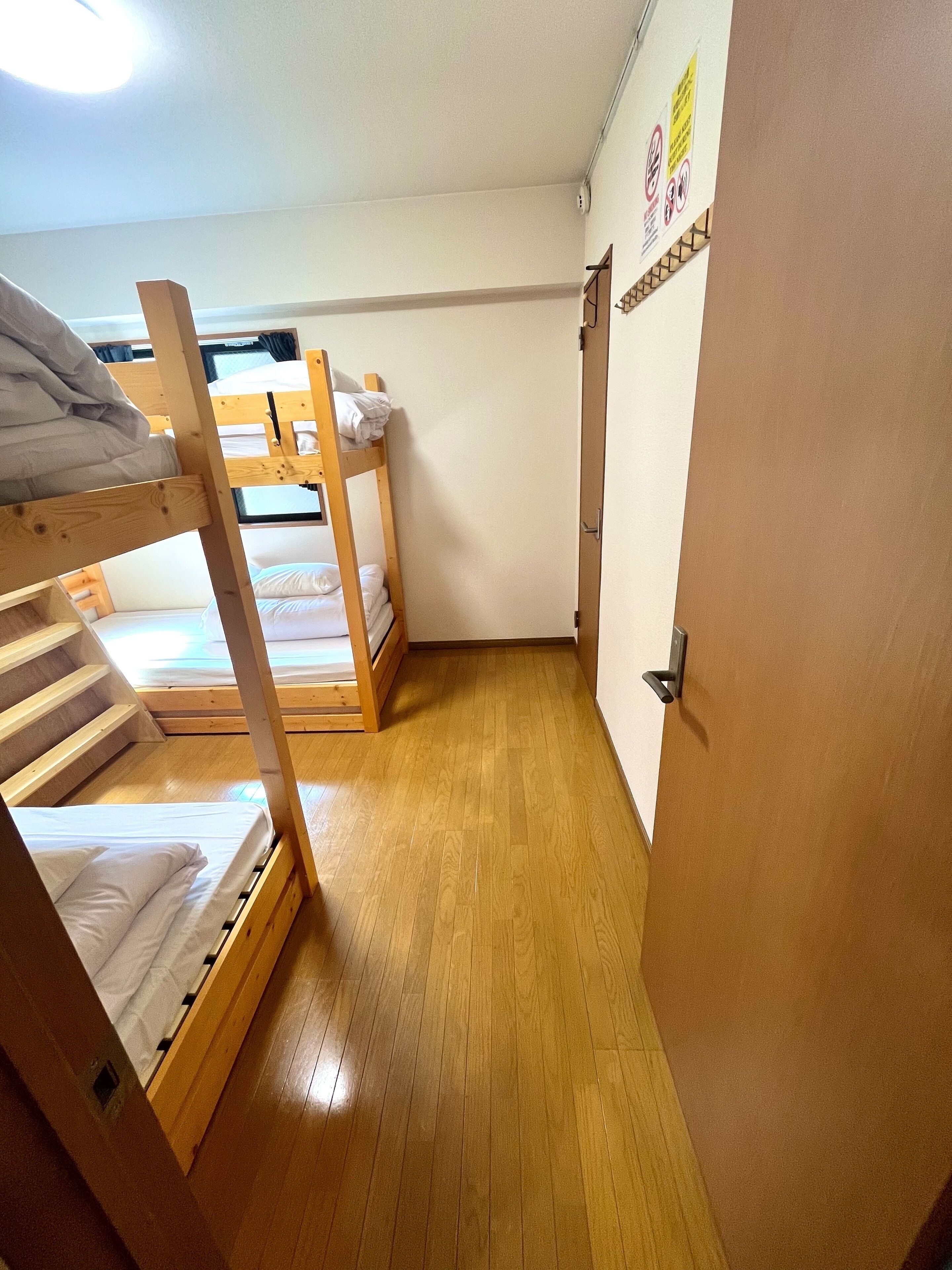 A dormitory room with bunk beds, wooden flooring, and a door with a handle.
