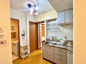 A compact kitchen with a sink, countertop, and cabinets. There is a sign on the wall and a door leading to another room. - SF Heights (Tokyo)