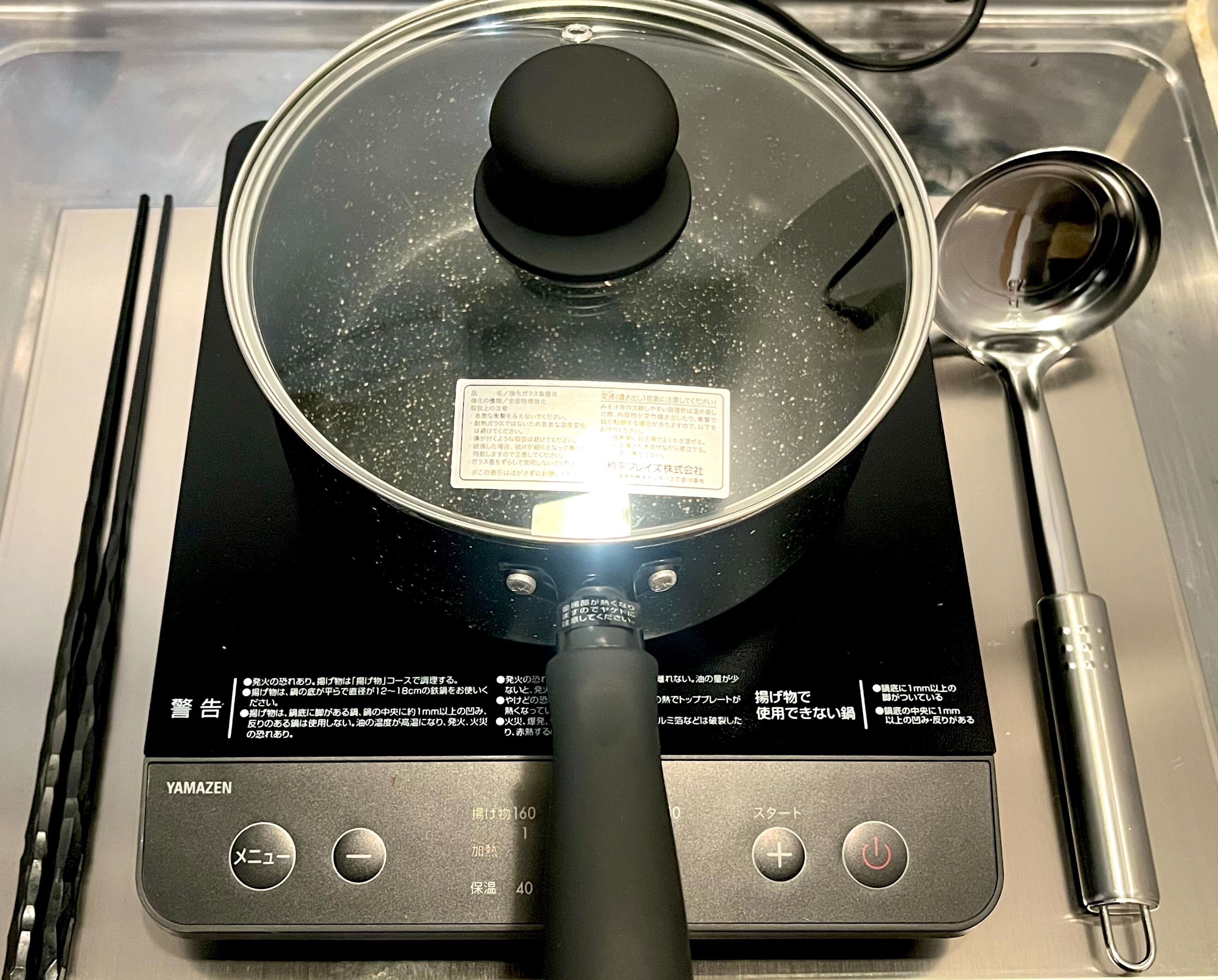 A kitchen with a pot on an induction cooktop, a ladle, and a black handle.
