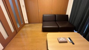 Una stanza con pavimento in legno, un divano, un tavolo con telecomando e una porta scorrevole con pannelli vetro smerigliato.