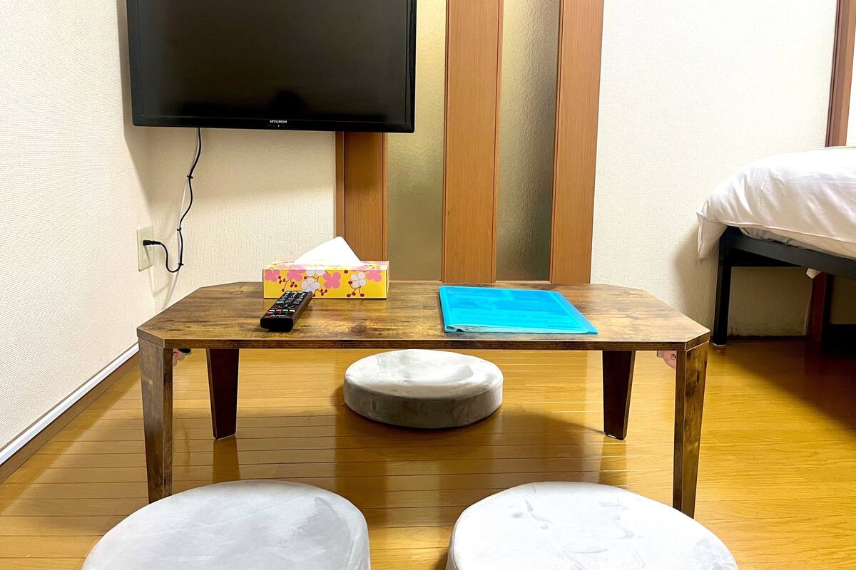A hotel room with a wooden table, a remote control, a tissue box, and a blue folder.