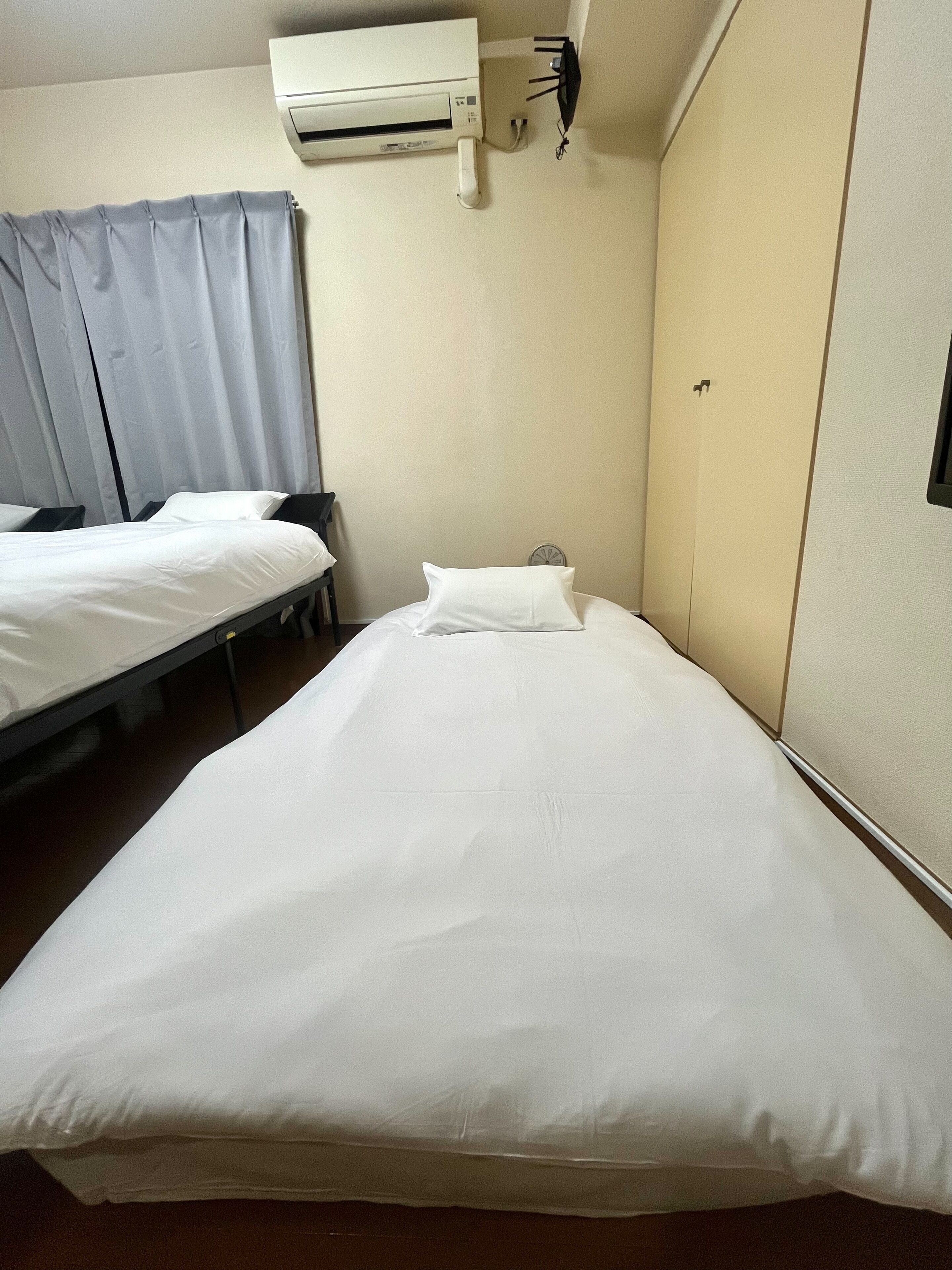 Ett hotellrum med två separata sängar, en väggmonterad luftkonditioneringsanläggning och en liten väckarklocka på väggen.