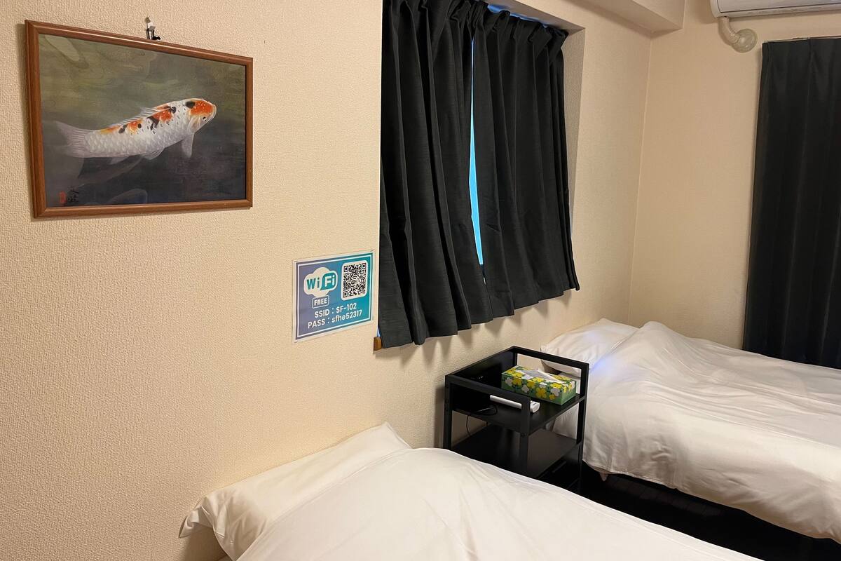 A hotel room with two beds, a painting of a fish, a Wi-Fi sign, and a window with black curtains.