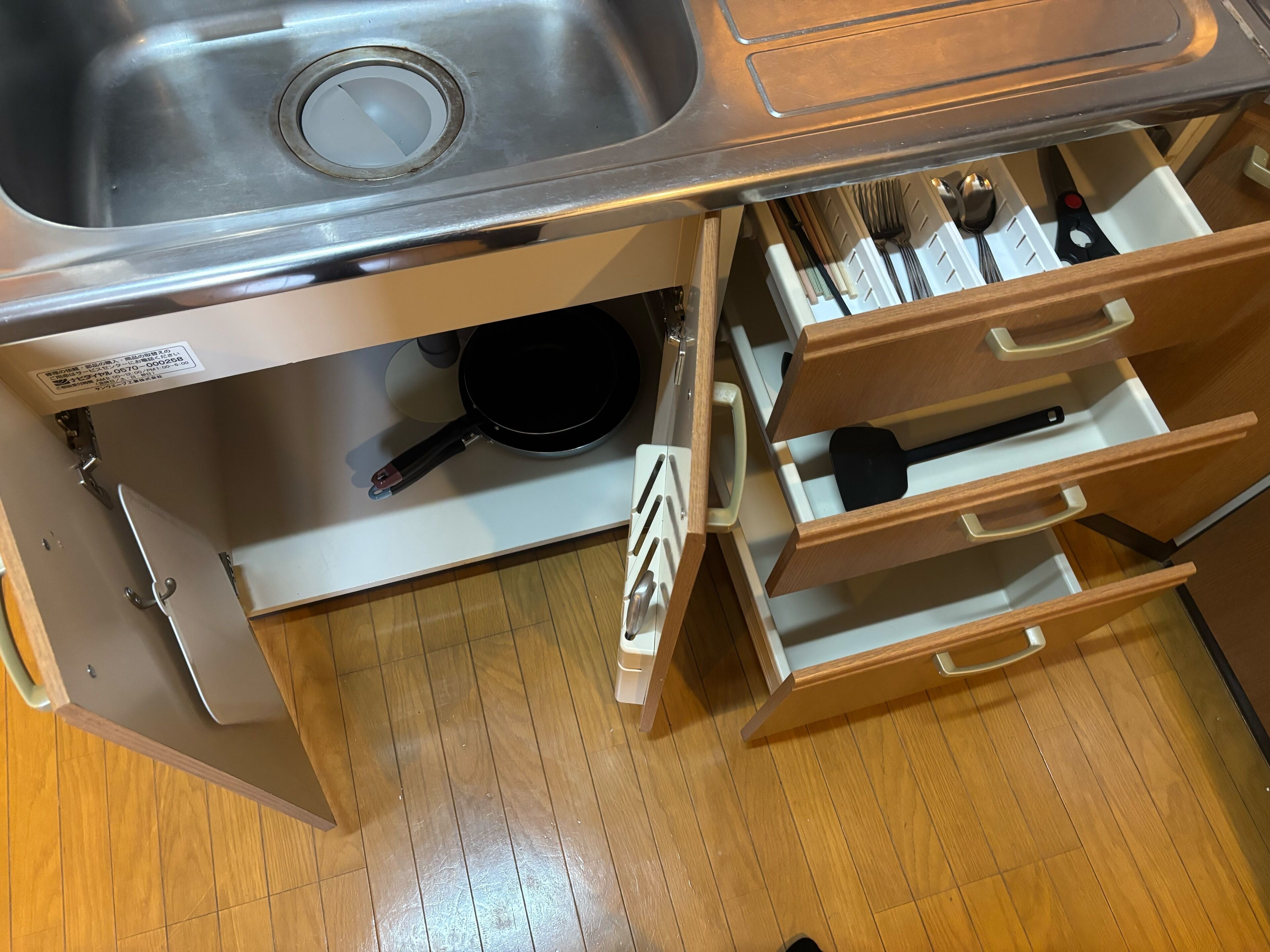 A kitchen with a stainless steel sink, wooden drawers, and a black frying pan.