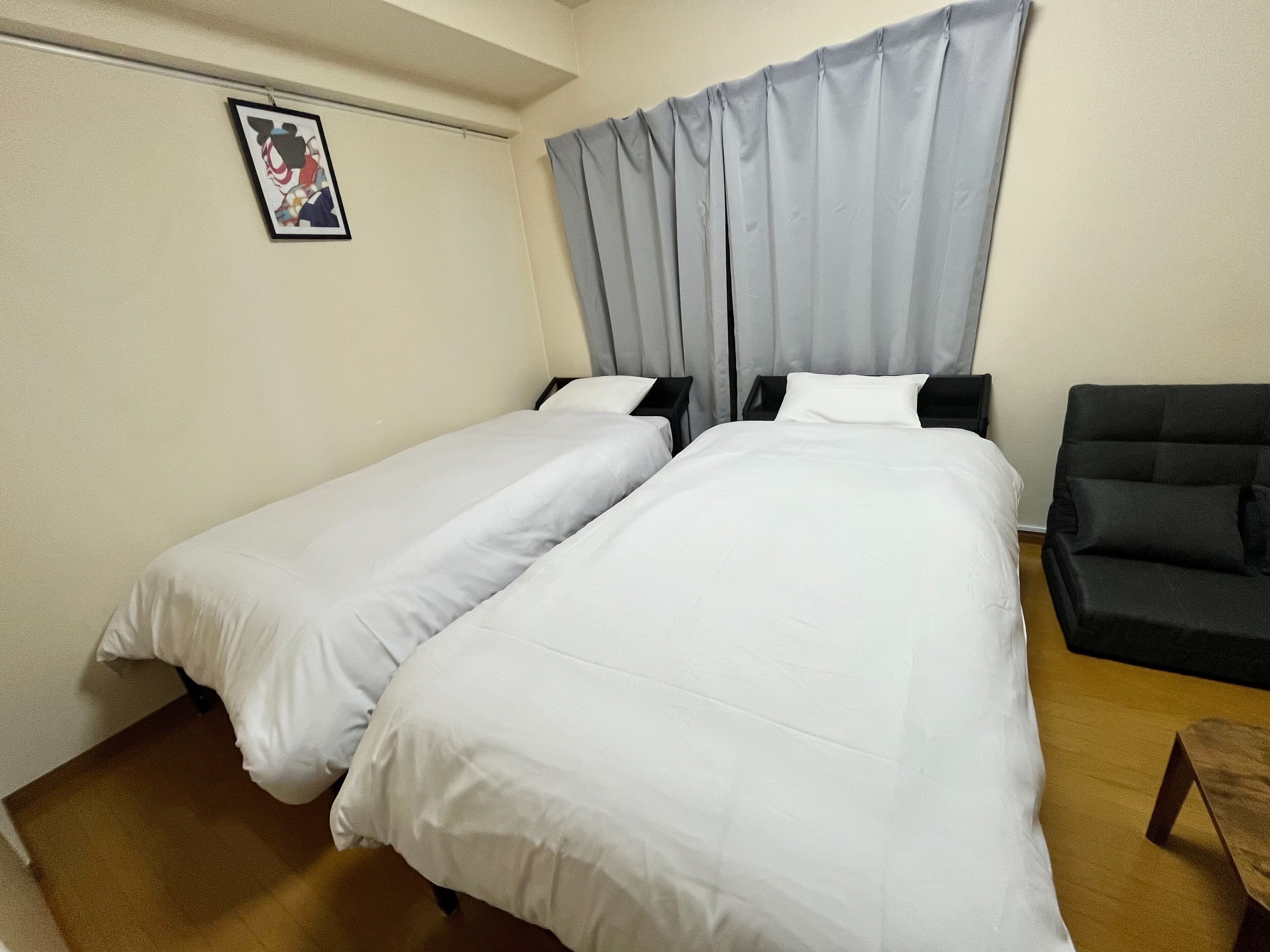 A hotel room with two single beds, a black armchair, and a small wooden table.