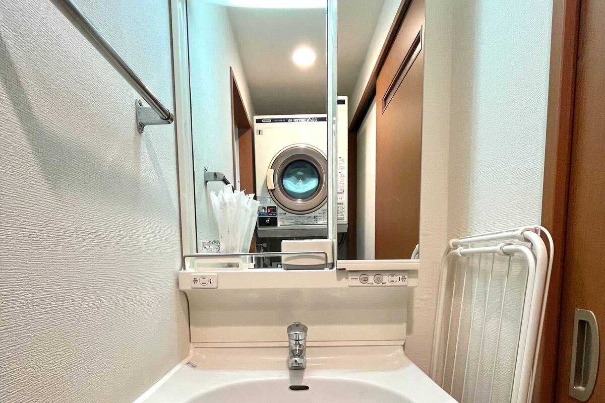 A bathroom with a sink, mirror, and a washing machine visible through the mirror.