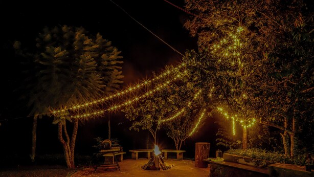 Een terras buiten bij nacht met een vuurkorf, een pad van stenen en lichtjes.