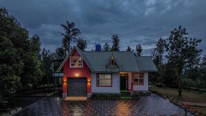 Een klein, laag huis met een rode en witte gevel, een schuin dak en een zichtbare waterreservoir op het dak.