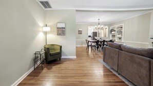 A spacious living area with a green armchair, a brown sofa, a dining table with chairs, and a chandelier.