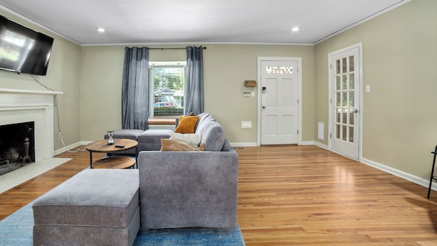A spacious living room with a fireplace, a grey sofa, a coffee table, and a flat-screen TV mounted on the wall.