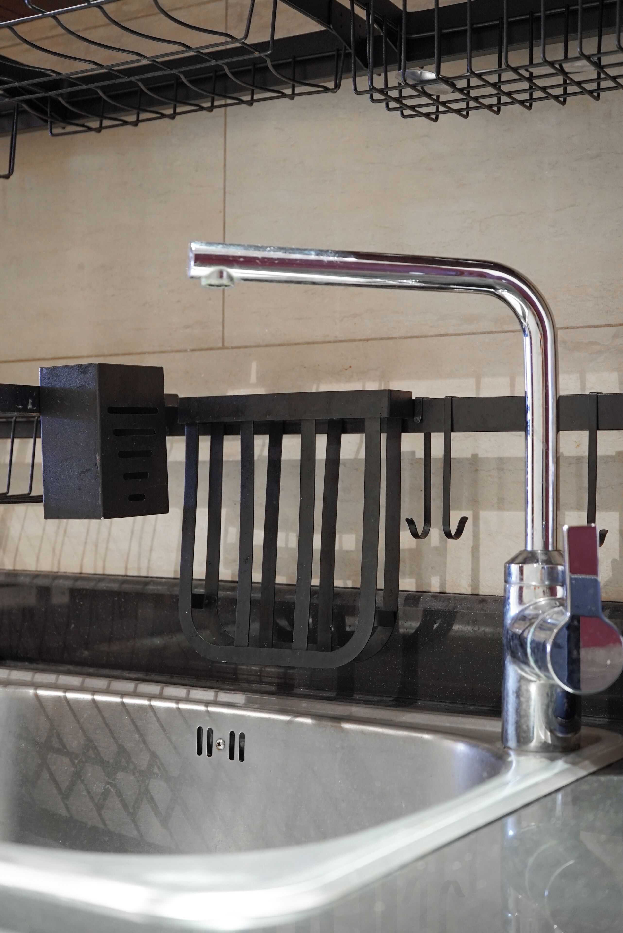 A kitchen sink with a modern faucet, a black soap dispenser, and a metal rack above the sink.