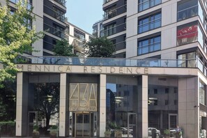 A modern building with a large glass entrance and the name "MENNICA RESIDENCE" displayed above. - Lumina 4-room apart in Mennica Residence (Warsaw)