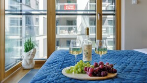 Una cama con un edredón azul, un plato de uvas y dos copas de vino junto a una botella de vino blanco sobre un alféizar.