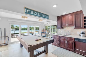 A pool table in a spacious room with a view of a pool and outdoor seating.