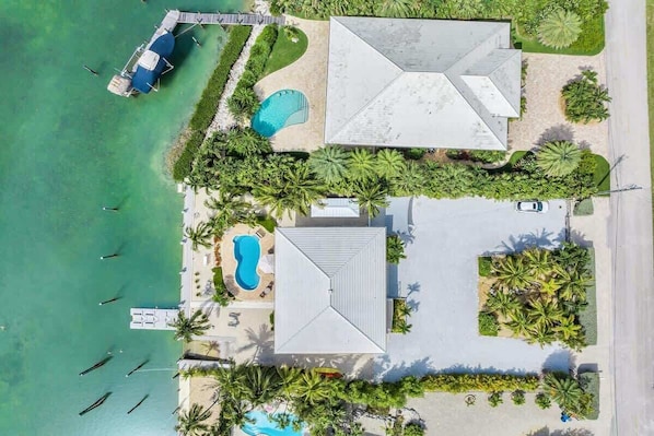 An aerial view of a resort with a large house, a swimming pool, and a dock with boats.