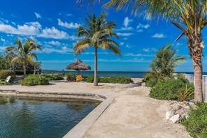 A beachfront resort with a pool, palm trees, and a thatched-roof hut.