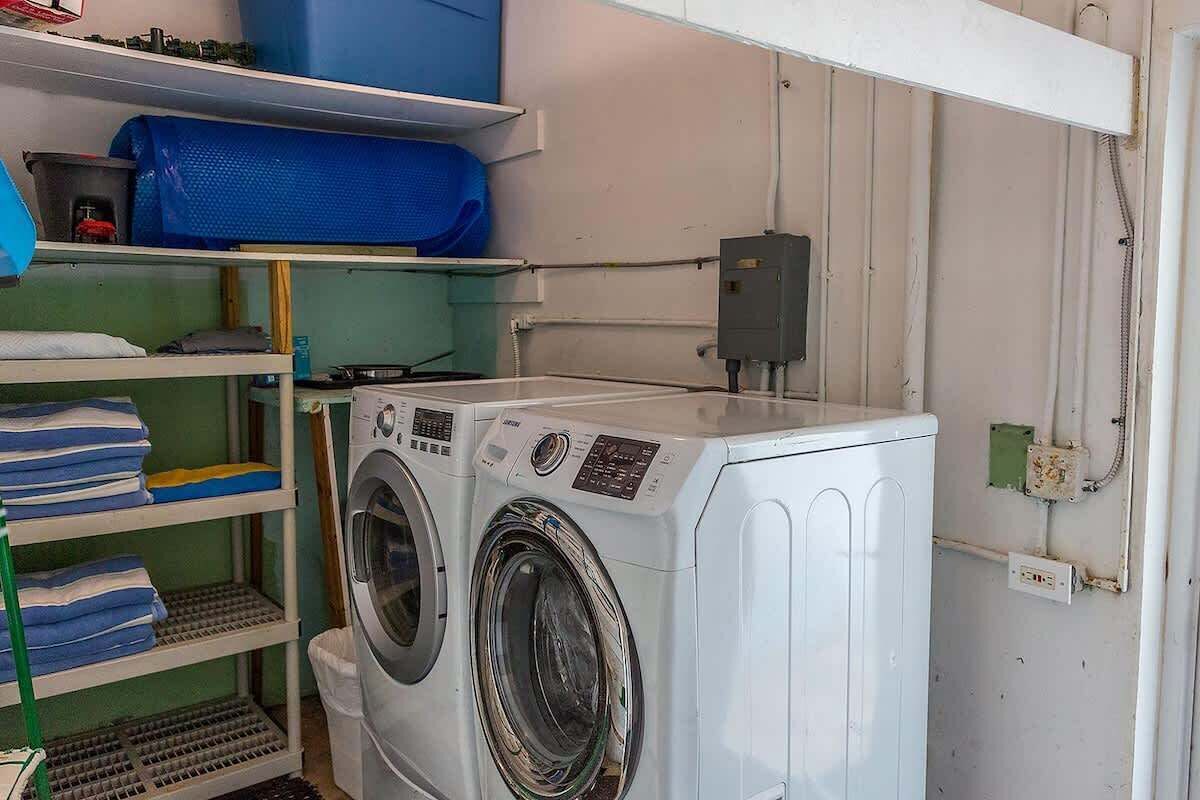 Een wasruimte met een wasmachine, planken met opgevouwen kleding en een blauwe opbergbox.
