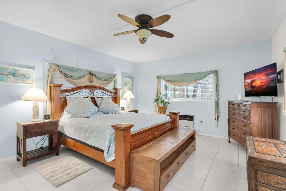 A bedroom with a wooden bed, a ceiling fan, a TV, and a dresser.