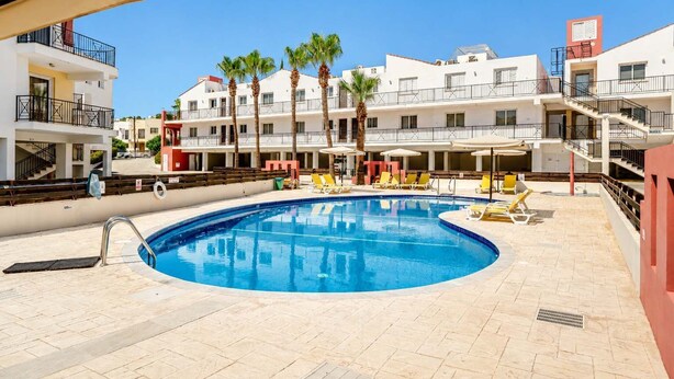 Una piscina con lettini, palme e un edificio a più piani con balconi.