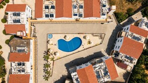 Vista aerea di una zona residenziale con piscina, diversi edifici con tetti in tegole rosse e un parcheggio.