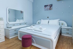 Un dormitorio con cama, tocador con espejo, mesita de noche y un taburete pequeño.