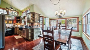 A spacious kitchen with wooden cabinets, a dining area with a large table, and a chandelier. - High Jinks - New Listing! (Cannon Beach)