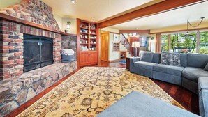 A living room with a fireplace, a bookshelf, a sofa, and a staircase leading to another level. - High Jinks - New Listing! (Cannon Beach)