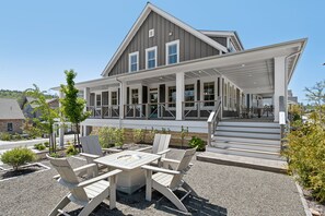 Een tweelaags huis met een overdekte veranda, buiten zitplaatsen en een vuurkuil.