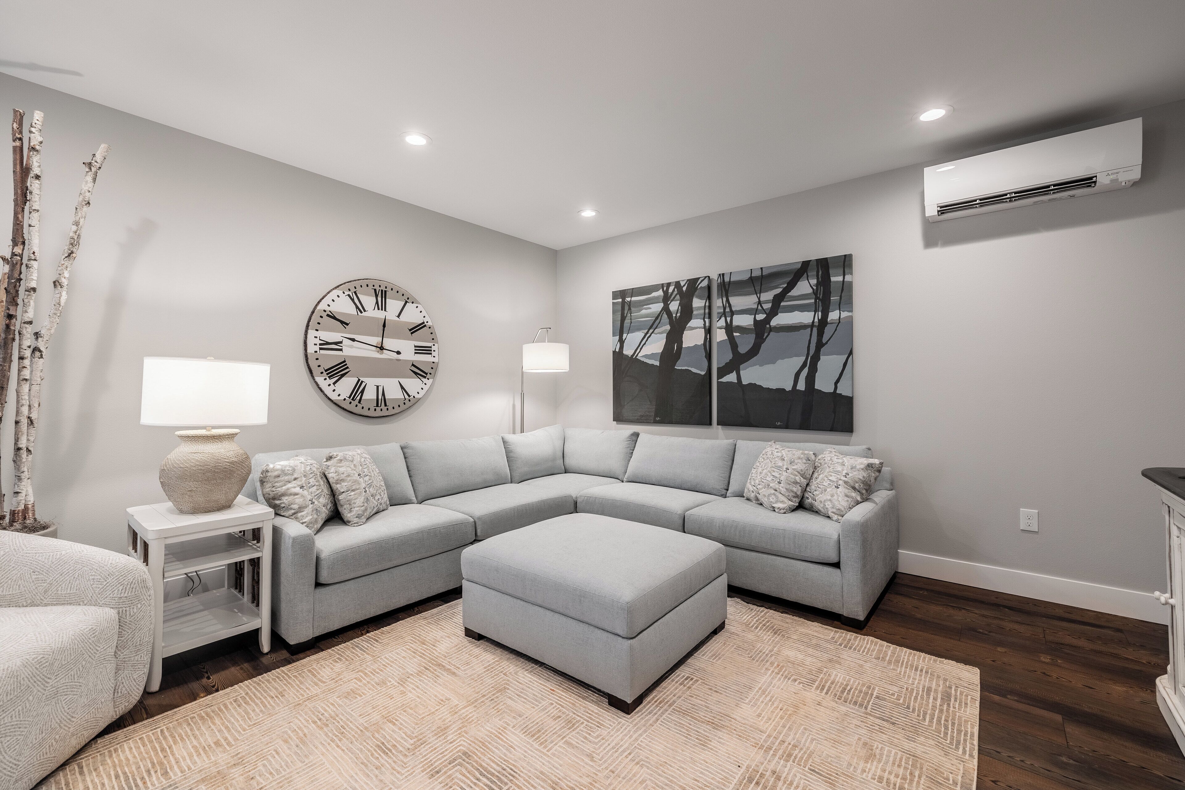 A modern living room with a grey sectional sofa, a round wall clock, a floor lamp, and a large abstract painting.