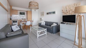 Ein modernes Wohnzimmer mit einem grauen Sofa, einem Couchtisch, einem Fernseher und einem Essbereich mit Tisch und Stühlen.