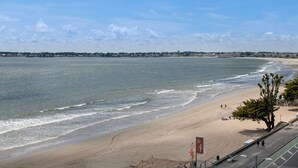Ein Strand mit freiem Blick auf das Meer, einem sandigen Ufer und einer Reihe von Gebäuden in der Ferne.