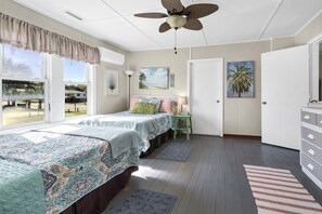 A bedroom with a bed, a ceiling fan, a window with curtains, a door, and a small table with a lamp. - OCEANFRONT, Four Bedroom 2 Bath Beach house ~ The Ravissant! (Edisto Island)