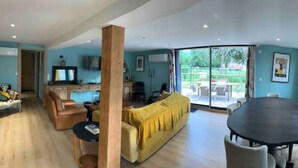 A spacious living area with a sofa, a dining table, and a TV. - Gite LE Passiflore (Beuvron-en-Auge)
