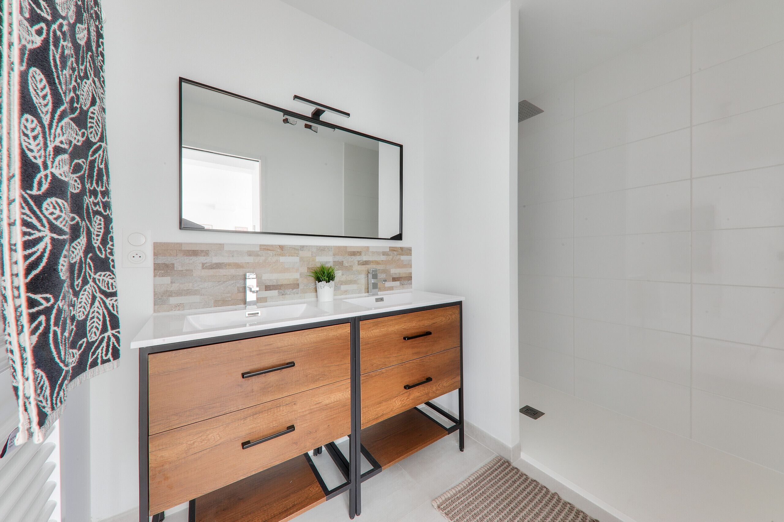 Een moderne badkamer met een witte wasbak, een houten opbergmeubel en een grote spiegel.