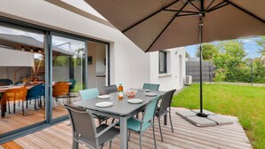 Un espace de restauration en plein air avec une table dressée pour quatre personnes, entourée de chaises, et protégée par un grand parasol.