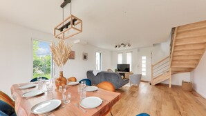 Un espace repas moderne avec une table en bois dressée pour quatre personnes, un canapé et un escalier.