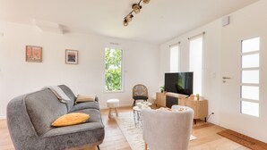 Un salon moderne avec un canapé gris, un fauteuil blanc, une table basse et un téléviseur à écran plat posé sur un meuble en bois.