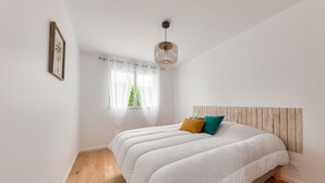 Une chambre à coucher avec un lit, une fenêtre avec des rideaux, une tête de lit en bois et un luminaire suspendu.