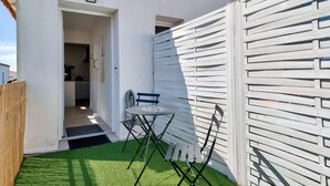 Un petit espace patio avec une table et des chaises, une clôture en bois et un mur blanc.