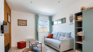Un salon moderne avec un canapé gris, un pouf rouge et un meuble en bois.
