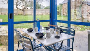 A table with various bowls, mugs, and a bottle, set against a blue-framed window overlooking a garden. - Quiet house for 6 - Less than 2km from the beach (Dinard)
