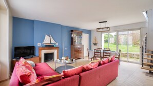 A living room with a red sofa, a television, a fireplace, and a dining area with a table and chairs. - Quiet house for 6 - Less than 2km from the beach (Dinard)