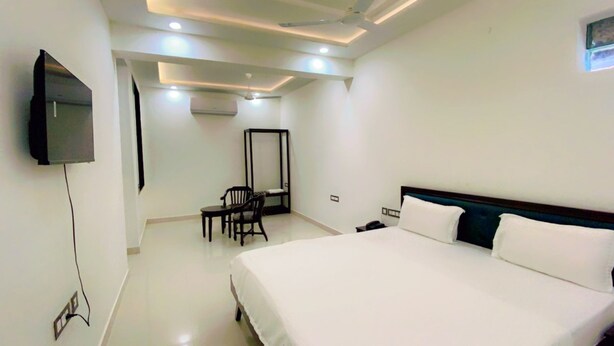A hotel room with a large bed, a desk with a chair, a TV mounted on the wall, and recessed ceiling lighting. - Hotel Giriraj Palace (Jaipur)